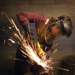student making sparks fly whil grinding metal with a safety mask on