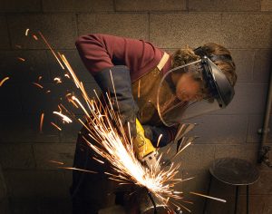 student making sparks fly whil grinding metal with a safety mask on