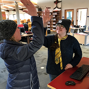 A pair of student workers at the Redwood Campus library give each other a high five.