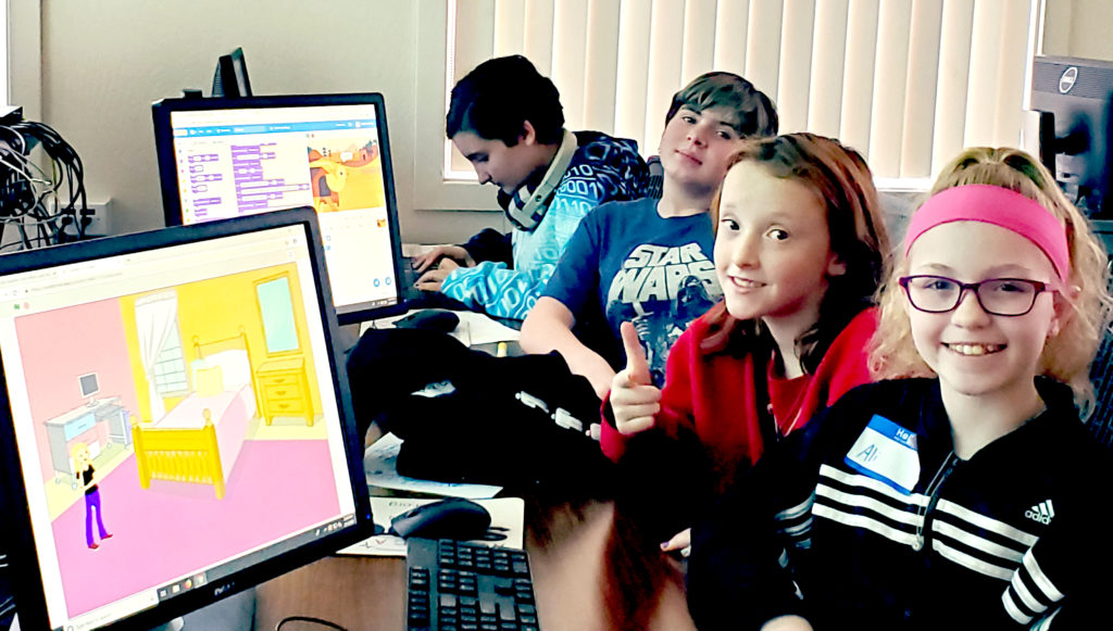 Four girls participating in the Girls Who Code camp are sitting at a table with computers.