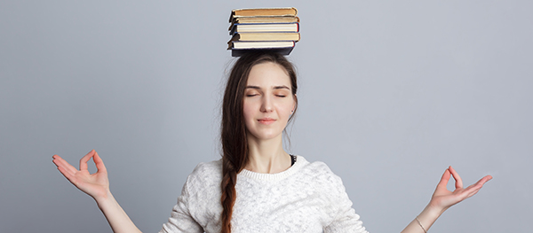 Stock photo of a young woman meditating with a stack of books balanced on her head.