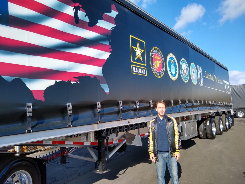 RCC Design & Digital Media student Wrenn Arbouin stands next to a TP Trucking trailer with a design he created honoring America's armed forces and veterans.