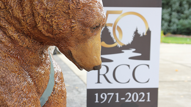 A picture of the bear sculpture in front of a sign that says RCC 1971-2021.
